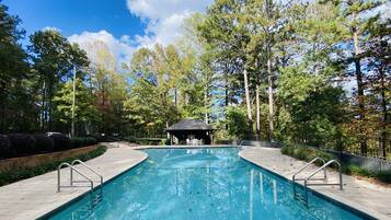 Une piscine rectangulaire avec des garde-corps en métal, entourée d’une allée pavée et d’arbres.
