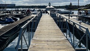 Un muelle de madera que conduce a un muelle con barcos y un faro a lo lejos.