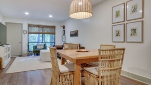 Un comedor con mesa de madera y sillas de mimbre, una lámpara colgante de fibra trenzada e impresiones botánicas enmarcadas en la pared.