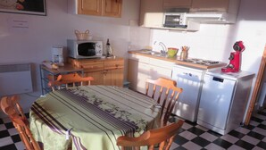 A compact kitchen with a dining table, chairs, a microwave, a sink, and a refrigerator. - Appartement Vacances (Gérardmer)