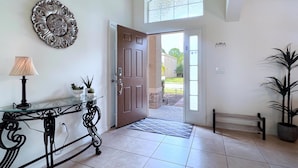 A hallway with a glass table, a lamp, a decorative plate, a door, and a potted plant.