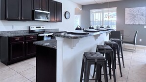 A modern kitchen with dark cabinets, a microwave, and a large island with bar stools.