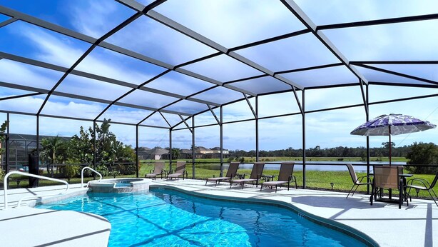 A covered outdoor swimming pool with clear blue water, surrounded by lounge chairs and a table with an umbrella.