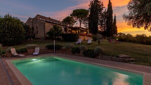 Une piscine avec des chaises longues, un bâtiment en pierre et un coucher de soleil en arrière-plan.