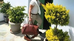 Un homme marchant en direction d’un bâtiment blanc avec une porte verte, portant un sac marron.