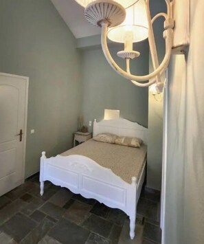 Quarto com cama branca, mesa de cabeceira, abajur e ventilador de teto.