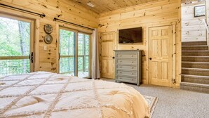A wooden cabin bedroom with a large bed, a dresser, and a staircase leading to another level. - Harper’s Hideaway- Close to Downtown Gatlinburg, Hot Tub, Guest Favorite! (Gatlinburg)