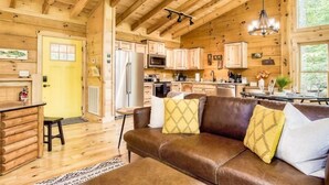 A log cabin interior with a kitchen, dining area, and a leather sofa with cushions. - Harper’s Hideaway- Close to Downtown Gatlinburg, Hot Tub, Guest Favorite! (Gatlinburg)