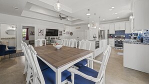 Een moderne keuken met witte kastjes, een centraal eiland en een eetgedeelte met een houten tafel en blauwe stoelen.