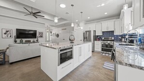 Een moderne keuken met witte kasten, een centraal eiland met oven, een ingebouwde magnetron en een groot raam boven de spoelbak.
