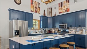 Een moderne keuken met blauwe kastjes, roestvrijstalen apparatuur en een groot kookeiland met krukken.