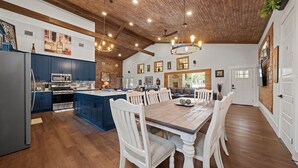 Een ruime keuken met houten kastjes, een groot eiland en een eethoek met een houten tafel en witte stoelen.