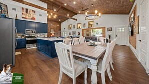 A spacious kitchen with a large island, wooden ceiling, and a dining area with white chairs.