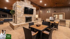 An outdoor patio with stone walls, a flat-screen TV, a fireplace, and a grill.