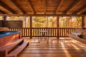 A wooden deck with a hot tub, a table with chairs, and a bench with a pillow.
