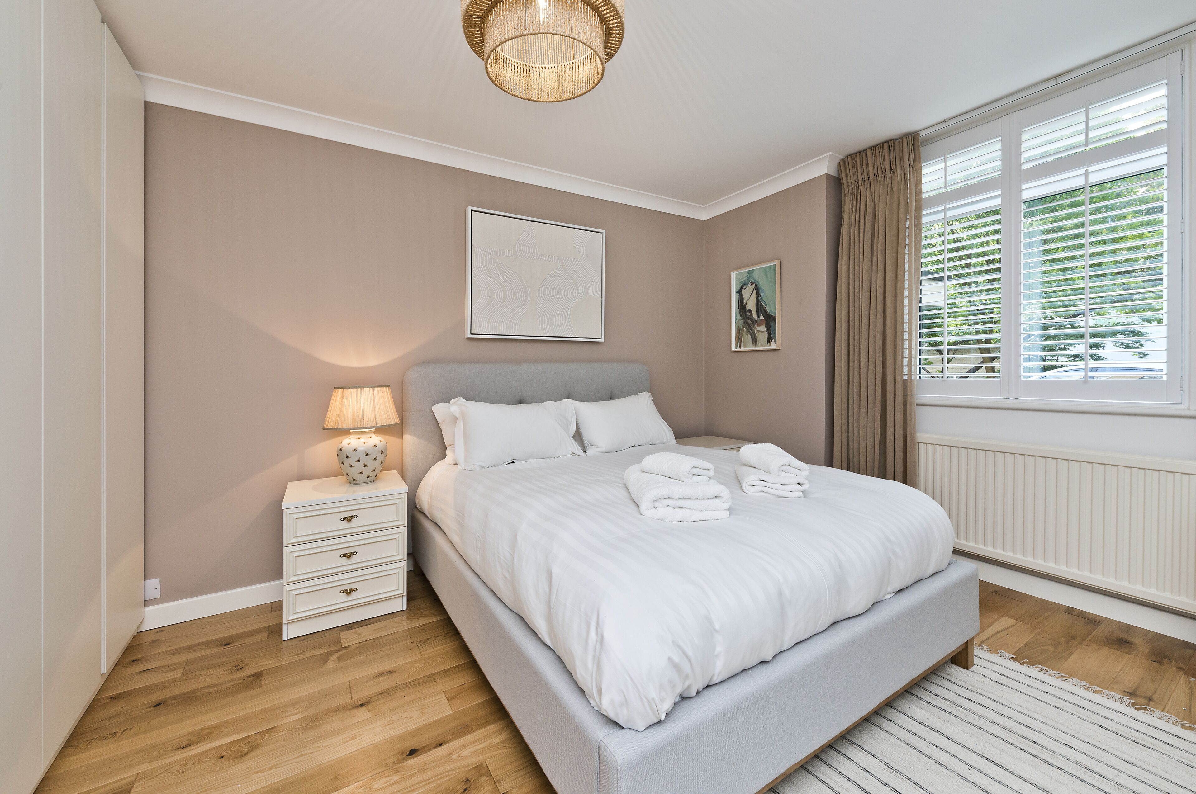 A bedroom with a bed, bedside table, lamp, and artwork on the wall.