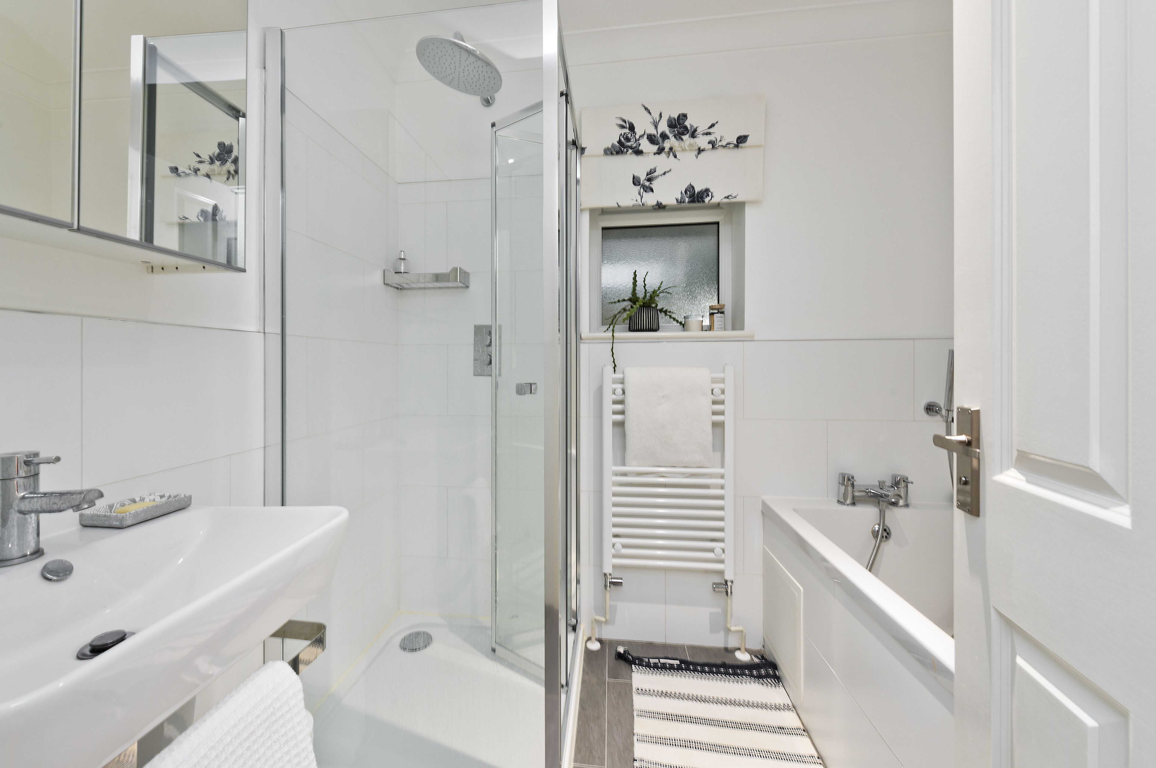 Un bany modern amb plat de dutxa envoltat de vidre, un lavabo blanc i una banyera.