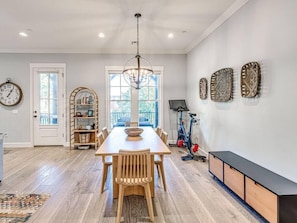 A dining area with a wooden table and chairs, a chandelier, a bookshelf, and exercise equipment. - Spacious + Central Condo in Carlton Landing (Carlton Landing)