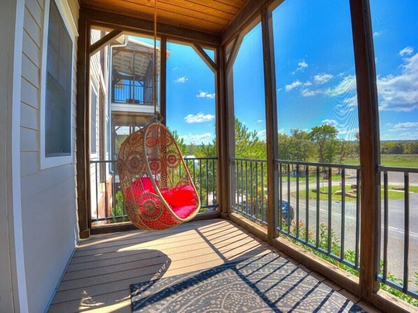A porch with a hanging chair, a view of the road, and a building in the background. - Spacious + Central Condo in Carlton Landing (Carlton Landing)