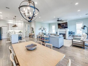 A modern kitchen with a central island, a dining area with a wooden table, and a living room with a sofa and fireplace. - Spacious + Central Condo in Carlton Landing (Carlton Landing)