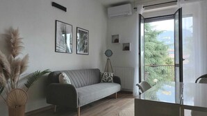 A modern living room with a grey sofa, a round table, and a balcony with a view of greenery. - Enrica apartment, elegant, near the lake historic center free parking (Lovere)