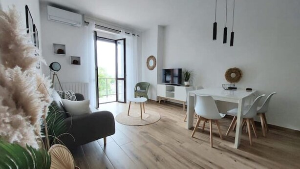 A modern living room with a sofa, a dining table with chairs, a TV, and a balcony with a view. - Enrica apartment, elegant, near the lake historic center free parking (Lovere)