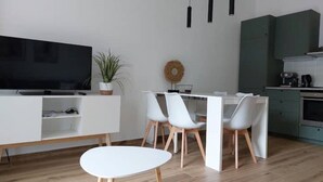 A modern kitchen with white cabinets, a dining area with white chairs, and a flat-screen TV on a white console. - Enrica apartment, elegant, near the lake historic center free parking (Lovere)