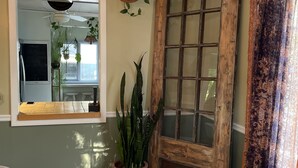 A room with a wooden door, a window with a view, a potted plant, and a white chair.