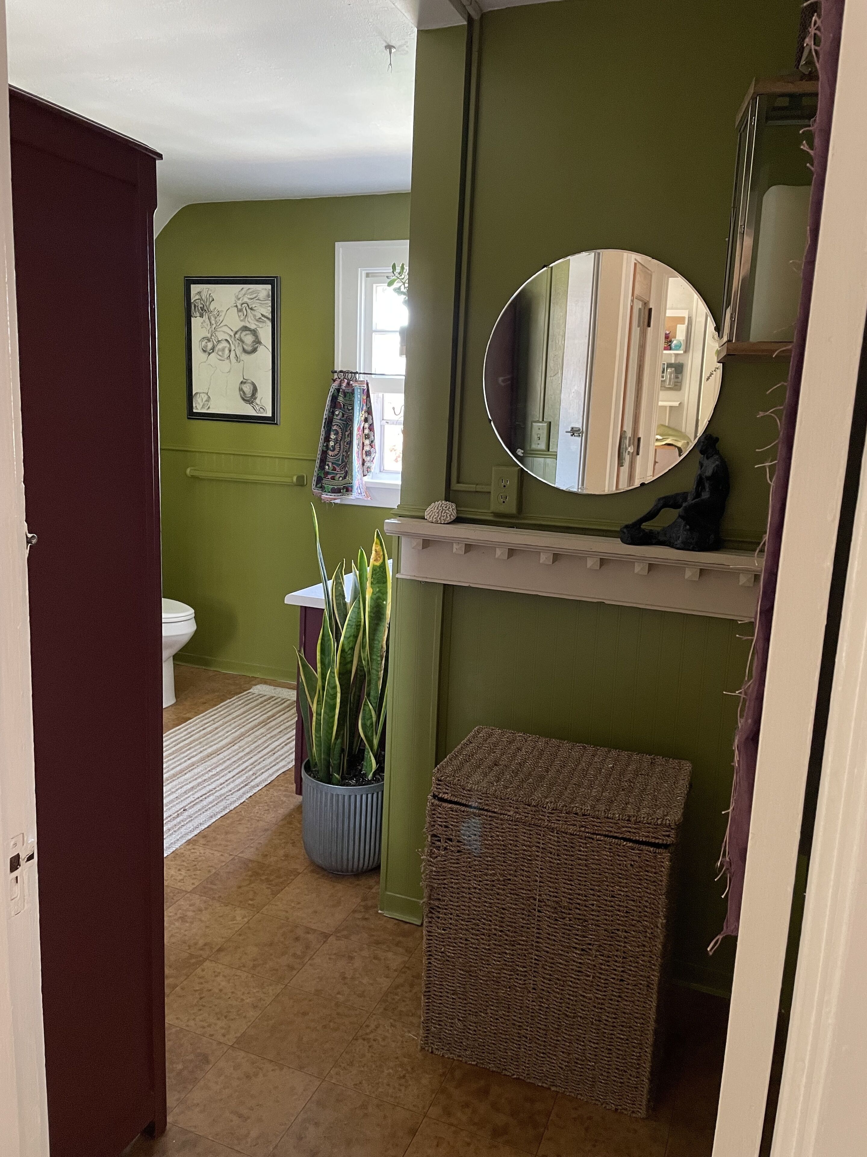 A bathroom with a toilet, a sink, a mirror, a potted plant, and a wicker basket.
