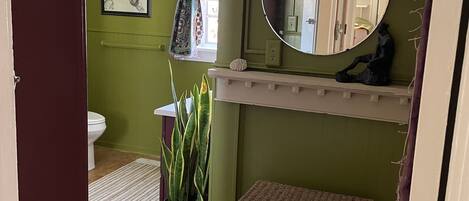 A bathroom with a toilet, a sink, a mirror, a potted plant, and a wicker basket.