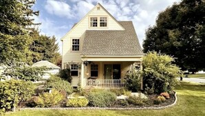 A two-story house with a front porch, surrounded by a well-maintained garden and trees.