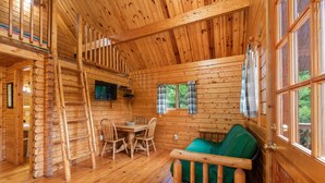 A wooden cabin interior with a dining area, a green sofa, and a staircase. - Riverfront! Mountain views 4 Miles to Luray Caverns  hot tub! at Line cabin (Luray)