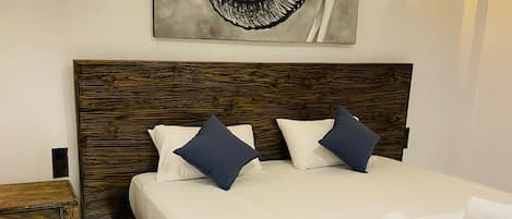Un dormitorio con cabecera de madera, una cama grande con ropa blanca, dos almohadas, una toalla enrollada y dos luces fijadas a la pared.