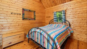 Dormitorio de cabaña de madera con cama, pequeño banco, ventana con vistas y espejo en la pared.