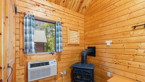 Interior de una cabaña de madera con ventana, un calentador en la pared y una estufa.