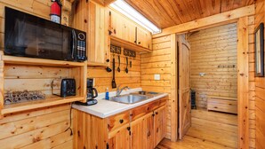 Una cocina de madera compacta con microondas, tostadora, pileta y utensilios colgantes.