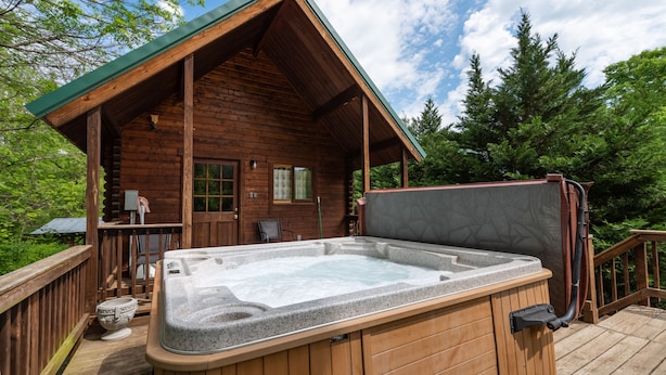 Una cabaña de madera con jacuzzi en la terraza, rodeada de árboles.