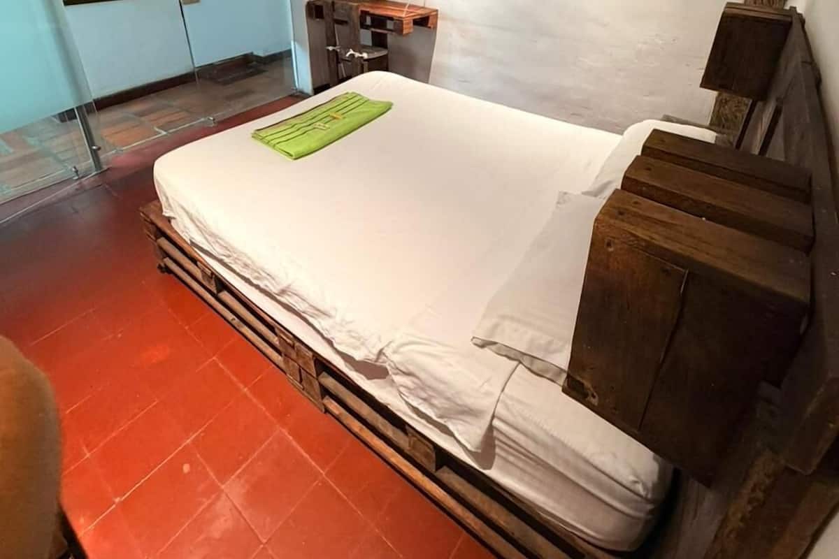 Une chambre avec un lit, une tête de lit en bois, une petite table et une étagère fixée au mur.