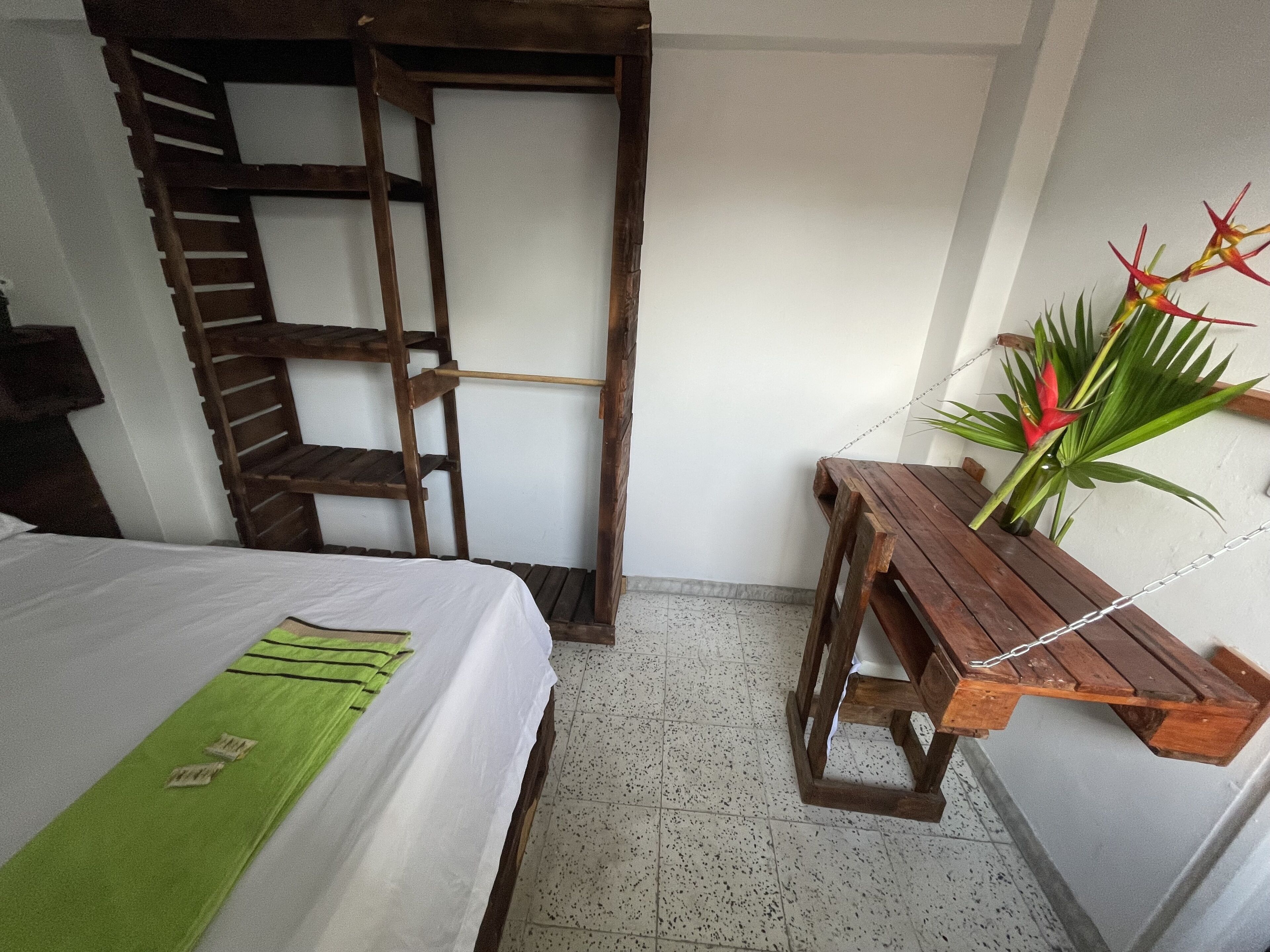 Una habitación con una cama, una escalera de madera, una pequeña mesa con una planta y una pared blanca.