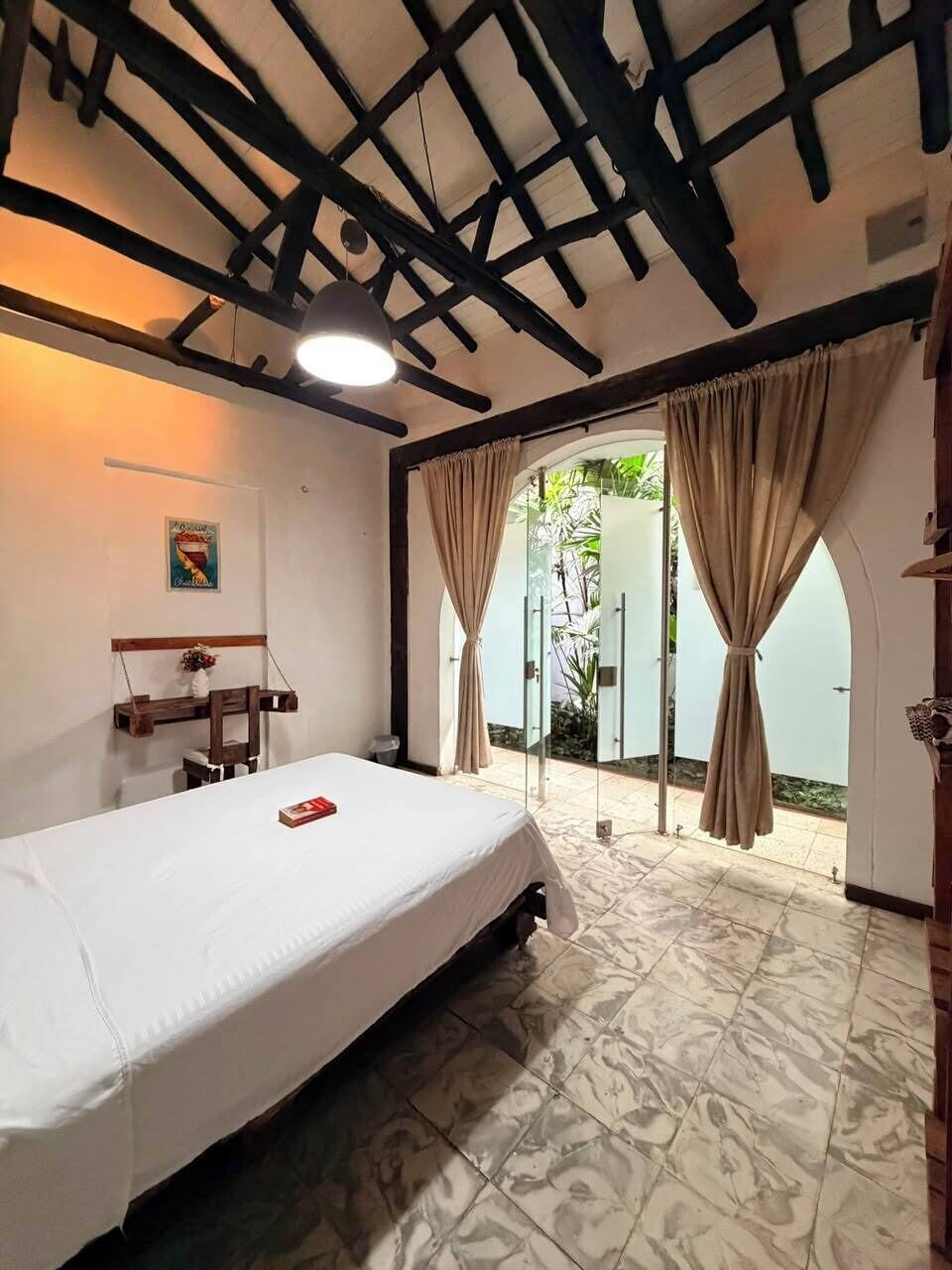 Un dormitorio con cama, una lámpara colgante, una silla de madera y vistas al exterior a través de un ventanal.
