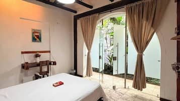 Un dormitorio con cama, una lámpara colgante, una silla de madera y vistas al exterior a través de un ventanal.