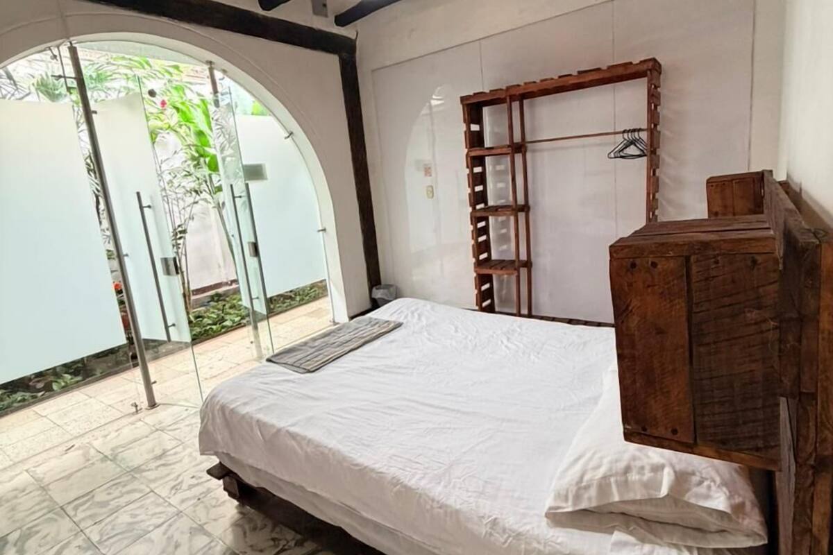 Une chambre à coucher avec un lit, une armoire en bois, un luminaire suspendu et une porte en verre donnant sur l’extérieur.
