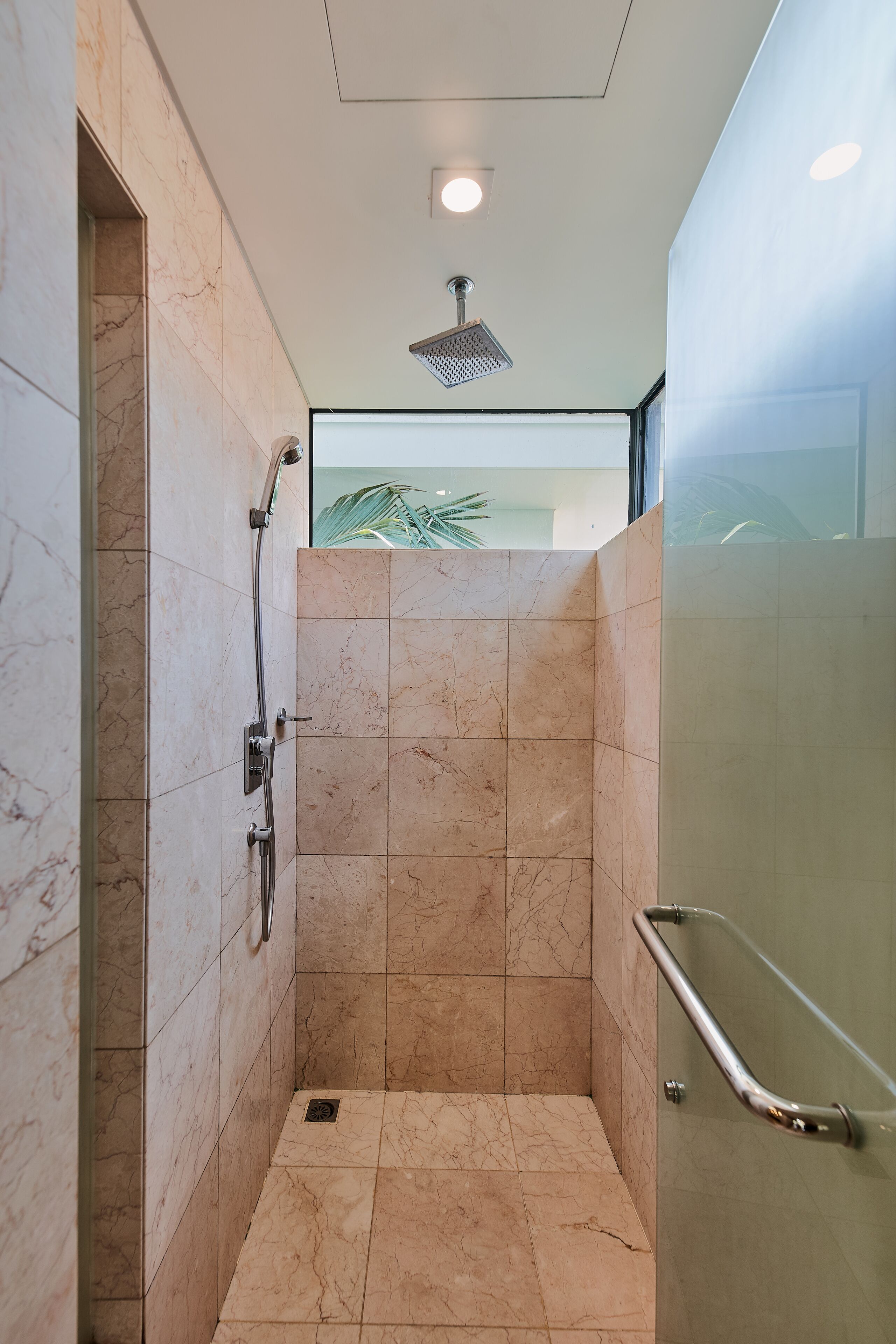 A modern bathroom with a shower, marble tiles, and a glass partition.