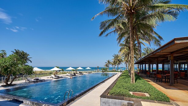 Un espace aménagé au bord de la piscine, avec des chaises longues, des parasols et une vue sur l’océan.