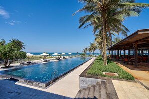 A poolside area with lounge chairs, umbrellas, and a view of the ocean. - The Ocean Luxury Villa Da Nang (Da Nang)