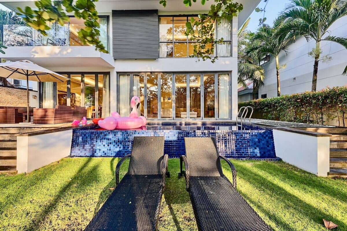 Una casa moderna con piscina, dos sillones de descanso y una decoración de flamenco rosa.