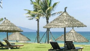 Une plage avec des parasols en chaume, des palmiers et des chaises longues.
