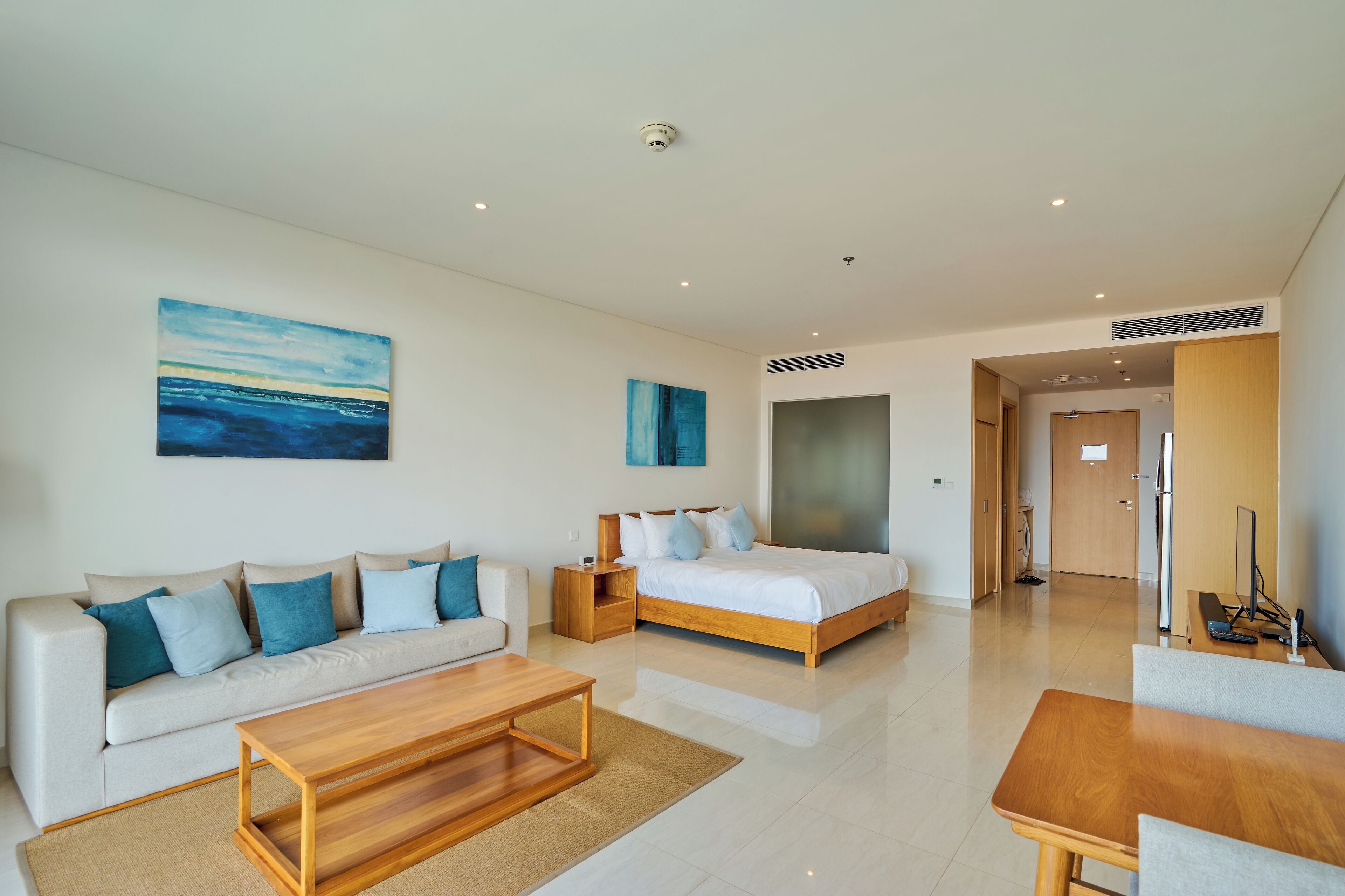 A modern hotel room with a sofa, a bed, a wooden coffee table, and a TV.