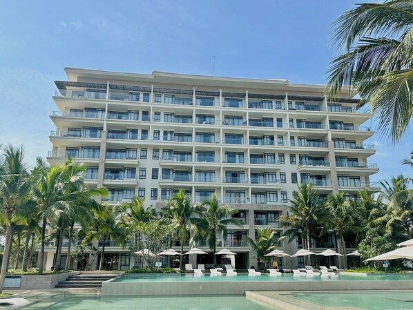 A multi-story hotel with a pool area, palm trees, and outdoor seating. - The Ocean Luxury Villa Da Nang (Da Nang)