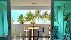 A balcony with a wooden table and chairs, a potted plant, and a view of the beach and palm trees. - Beautiful Caribbean Ocean View Gem ! Newly remodeled apartment.  (Luquillo)